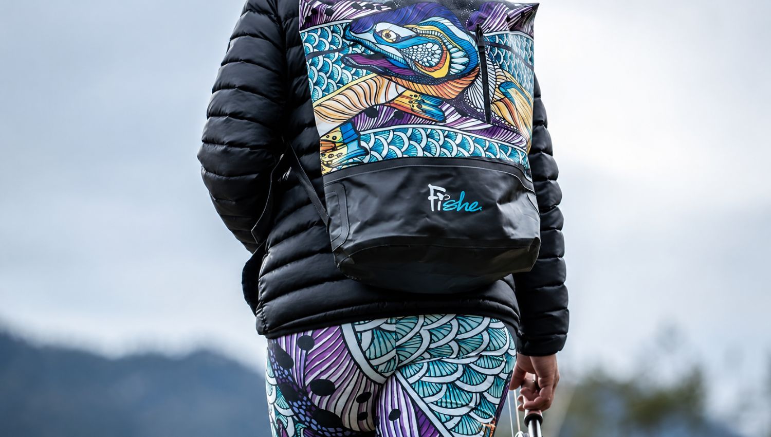 Person wearing a colorful backpack with a fish design and 'Fishe' branding, standing outdoors.