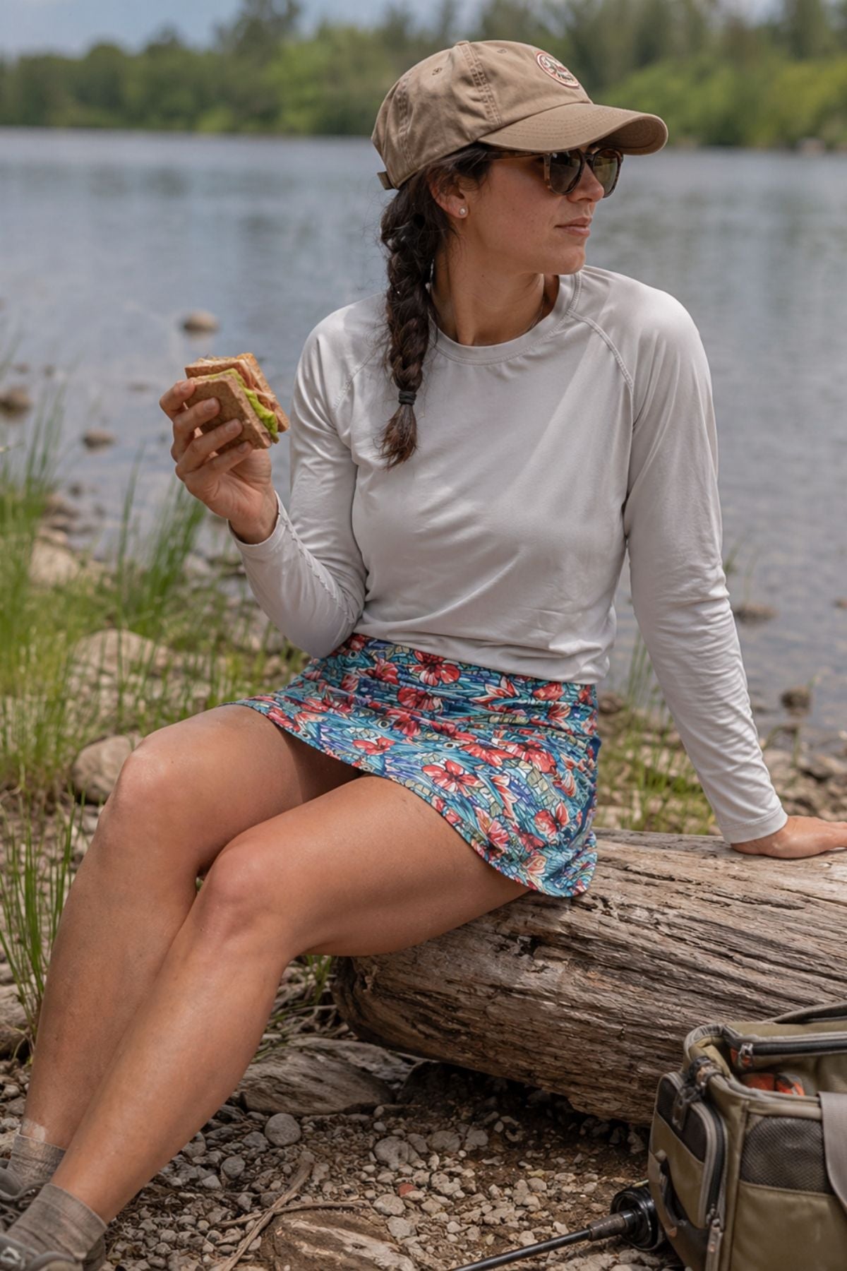 Woman sitting on a log by a lake, eating a sandwich