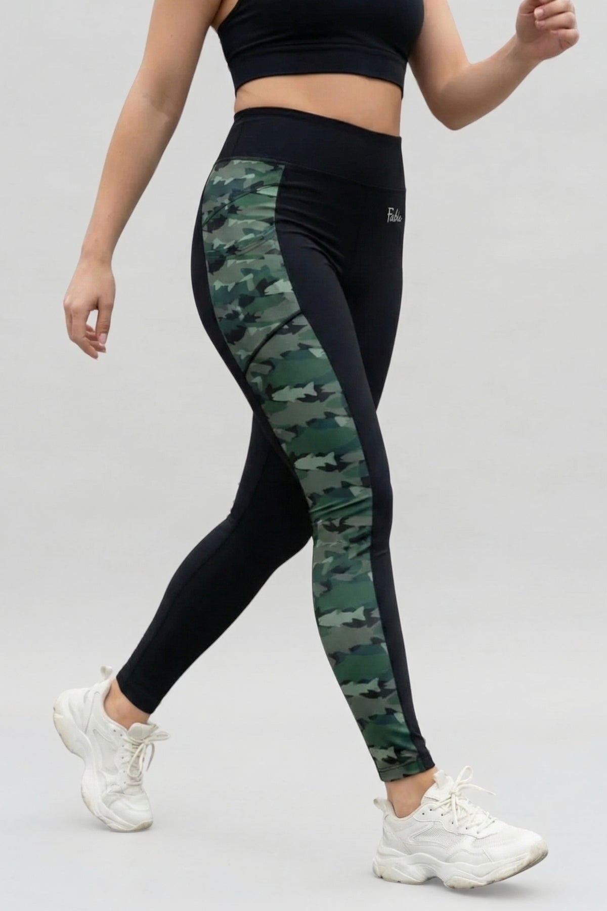 Person wearing black and green camouflage leggings on a light gray background