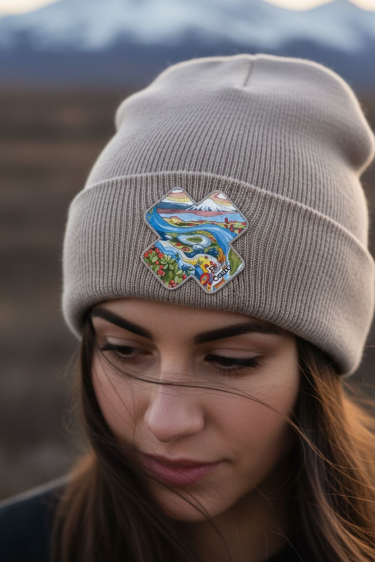 Person wearing a gray beanie with a colorful patch against a mountainous background