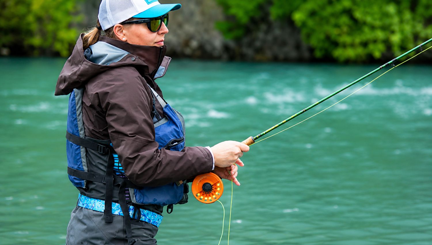Person fly fishing in a body of water wearing a life jacket and sunglasses.