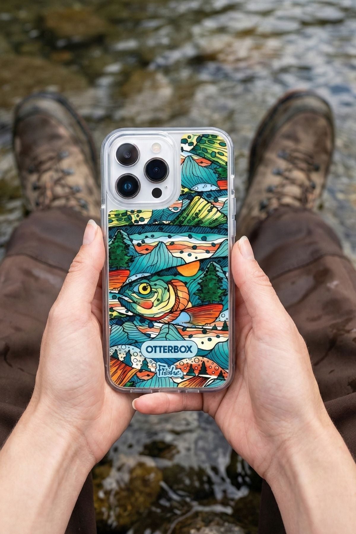 Person holding a phone with a colorful OtterBox case near a stream.