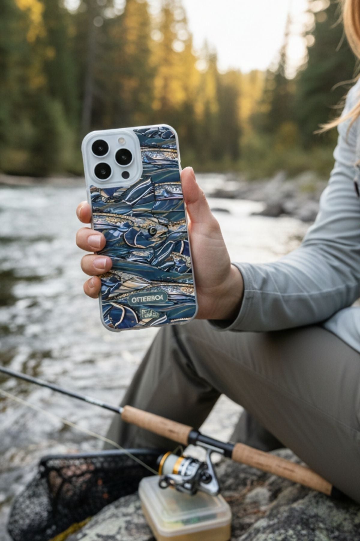 Person holding a phone with a fishing-themed case by a river