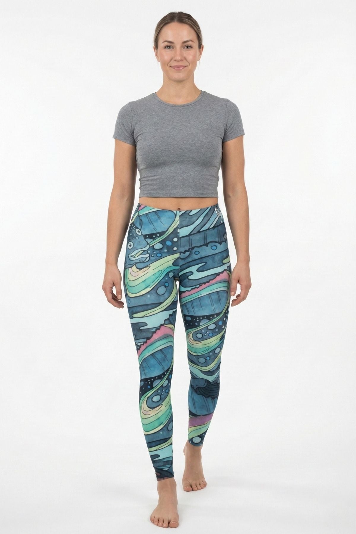Woman wearing colorful patterned leggings and a gray crop top on a white background