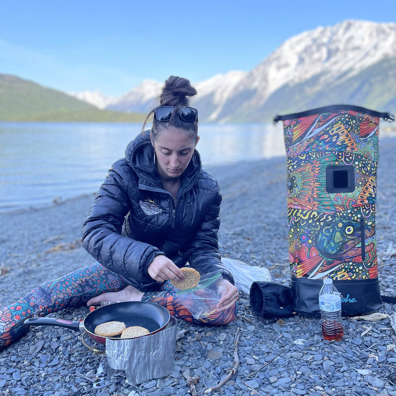 Woman preparing food beside a mountain lake with Fishe gear