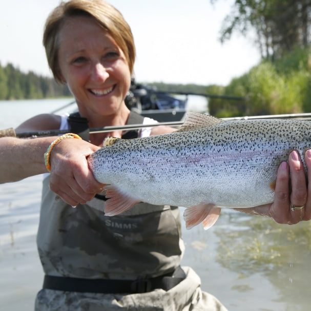 An angler holding a trout beside the river.