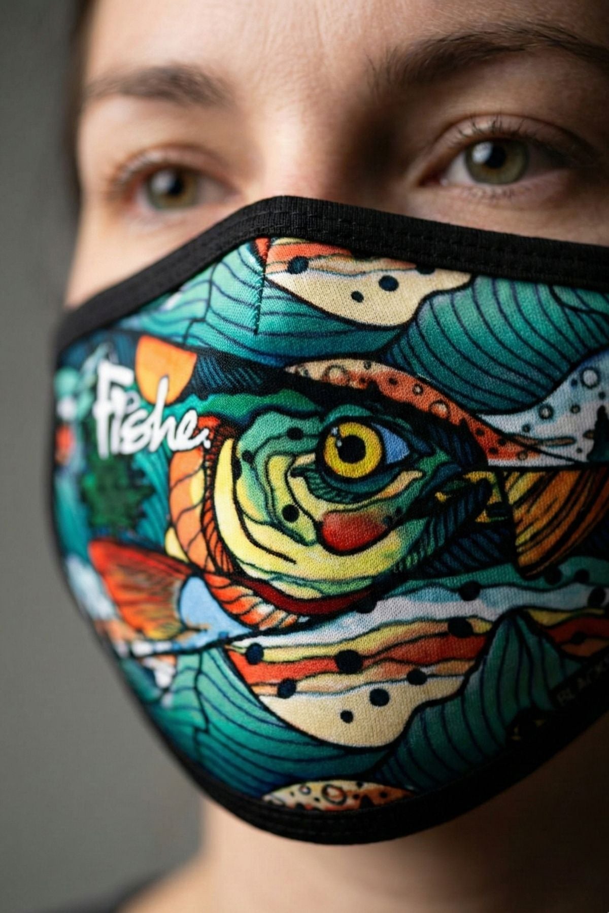 Colorful fish-themed face mask worn by a person against a neutral background