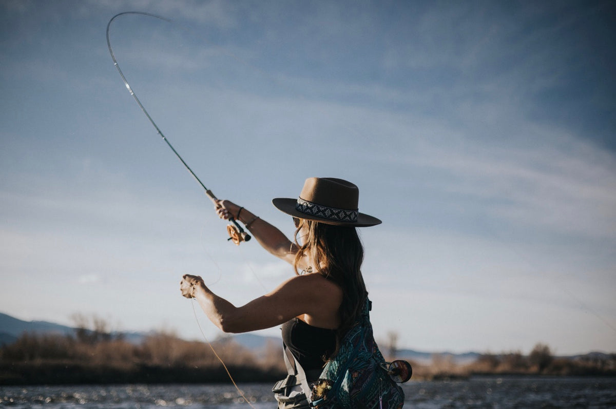 Woman in a wide-brim hat casting a fly rod on a river
