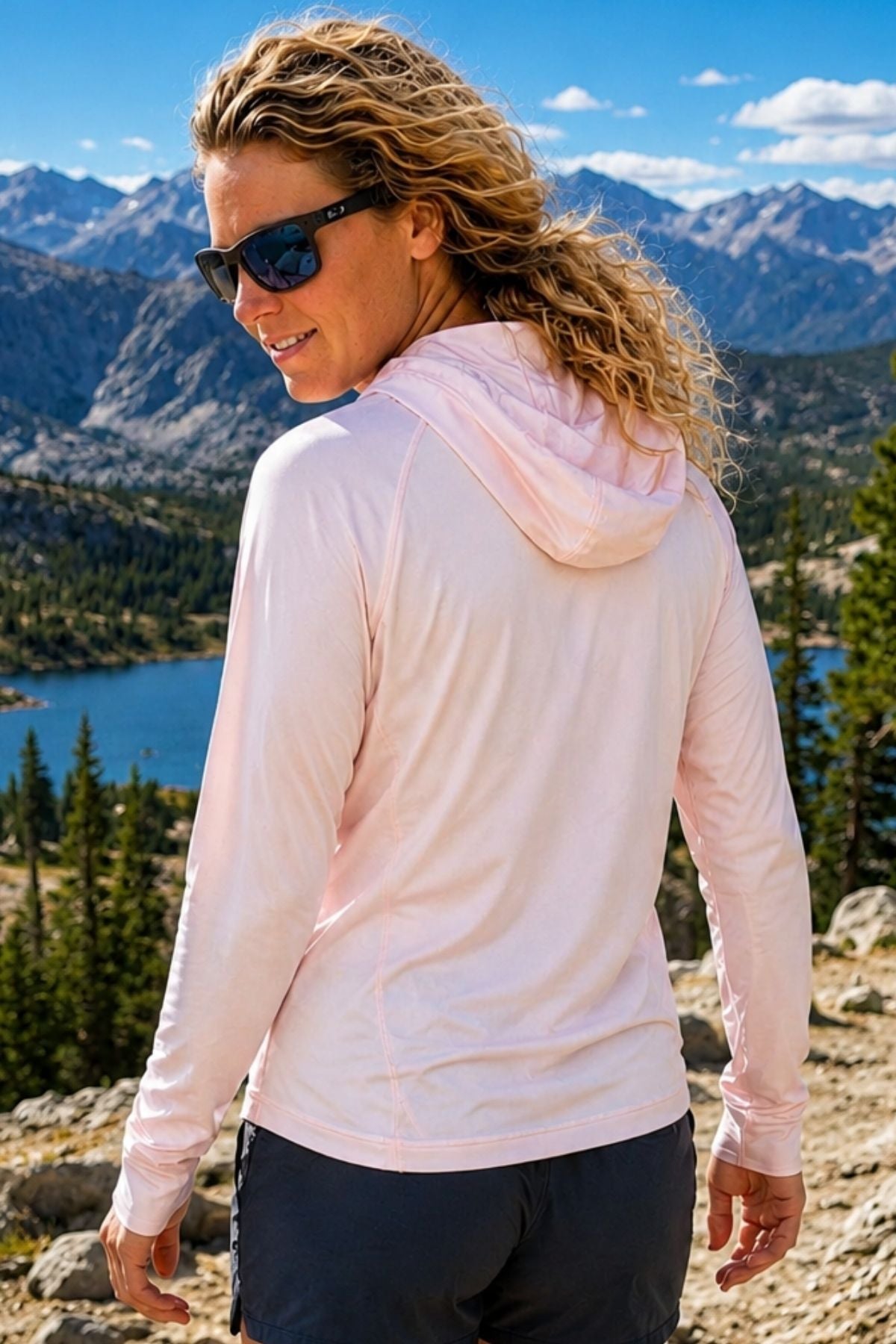 Woman wearing a light pink hoodie with a scenic mountain and lake background