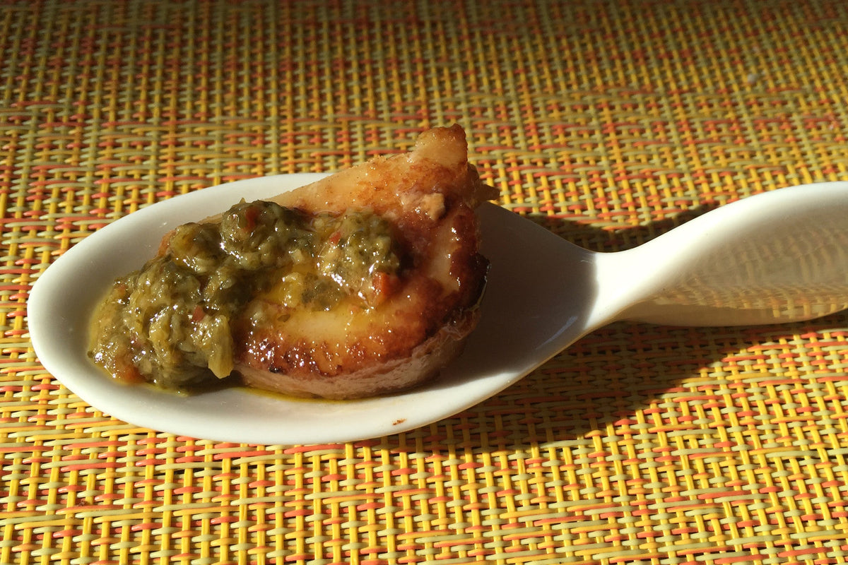 Cast-iron seared scallop topped with pesto in a serving spoon