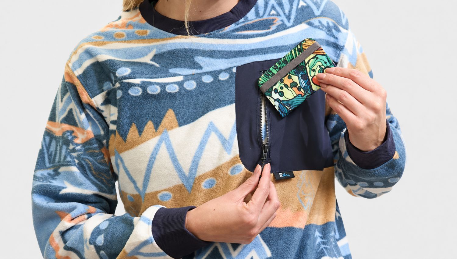 Person wearing a patterned sweater holding a colorful card against a plain background