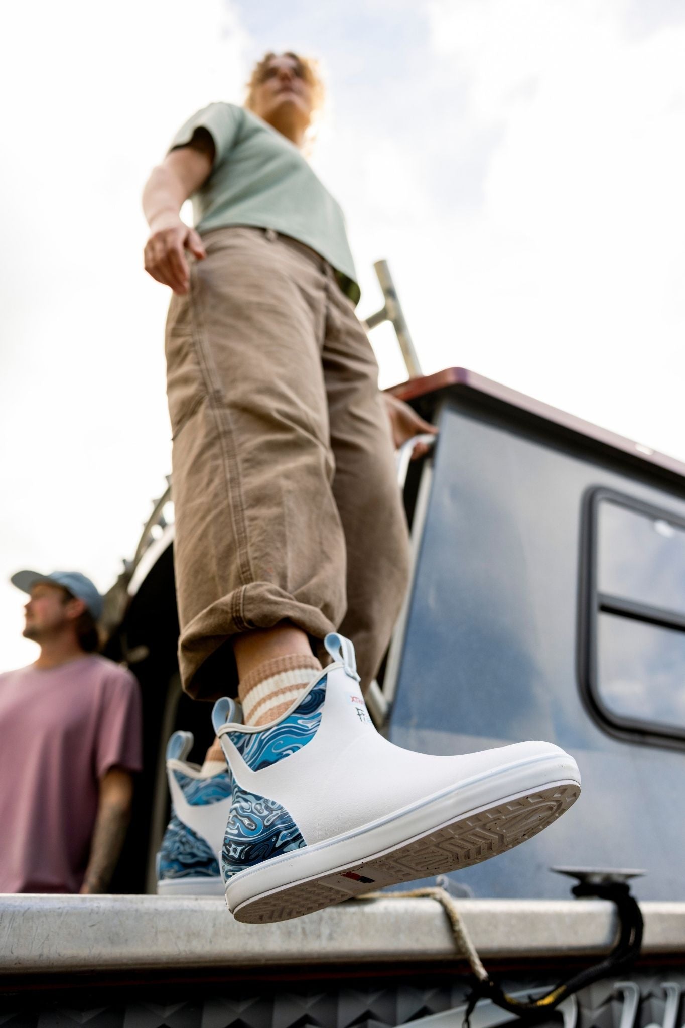 Person wearing white sneakers with blue patterns standing on a vehicle
