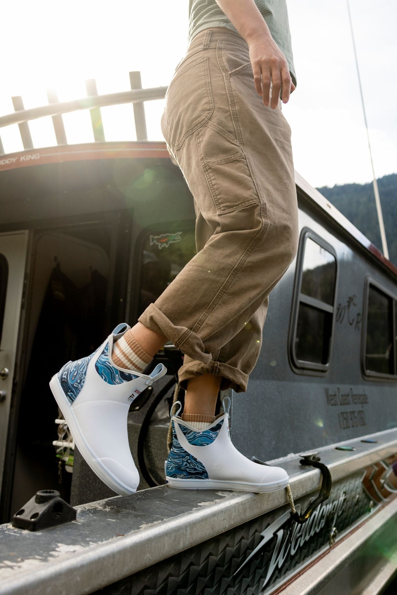Person wearing white sneakers with blue accents, standing on a vehicle's step.