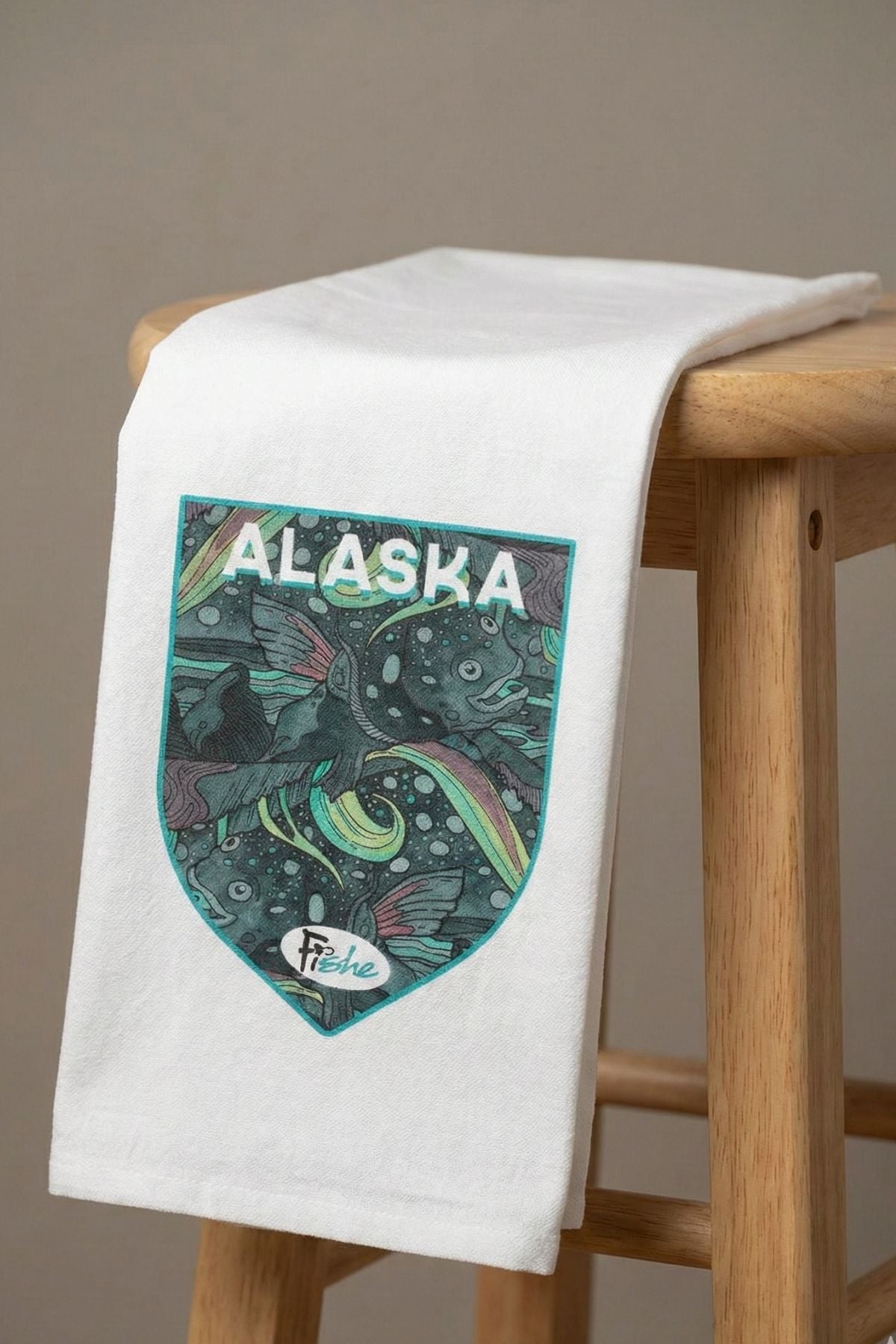 White towel with Alaska design on a wooden stool against a brown background