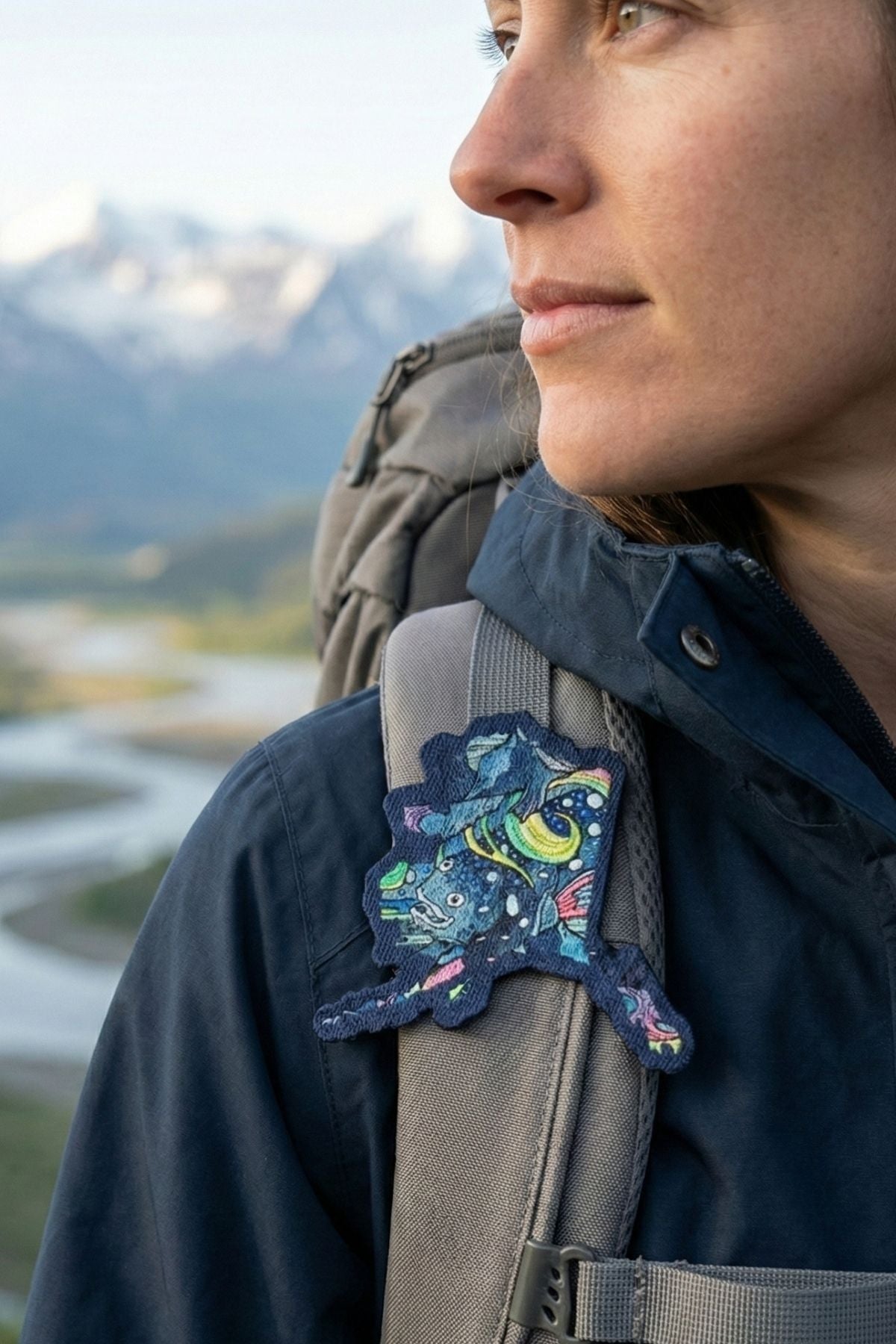 Person wearing a backpack with a colorful patch, standing in a mountainous landscape.