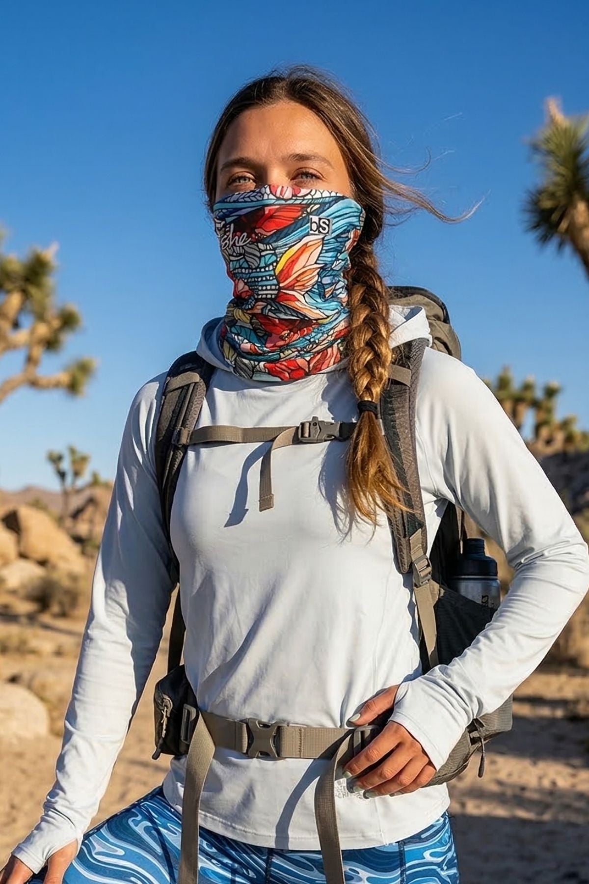 Person hiking in a desert landscape wearing a colorful face mask and white long-sleeve shirt.