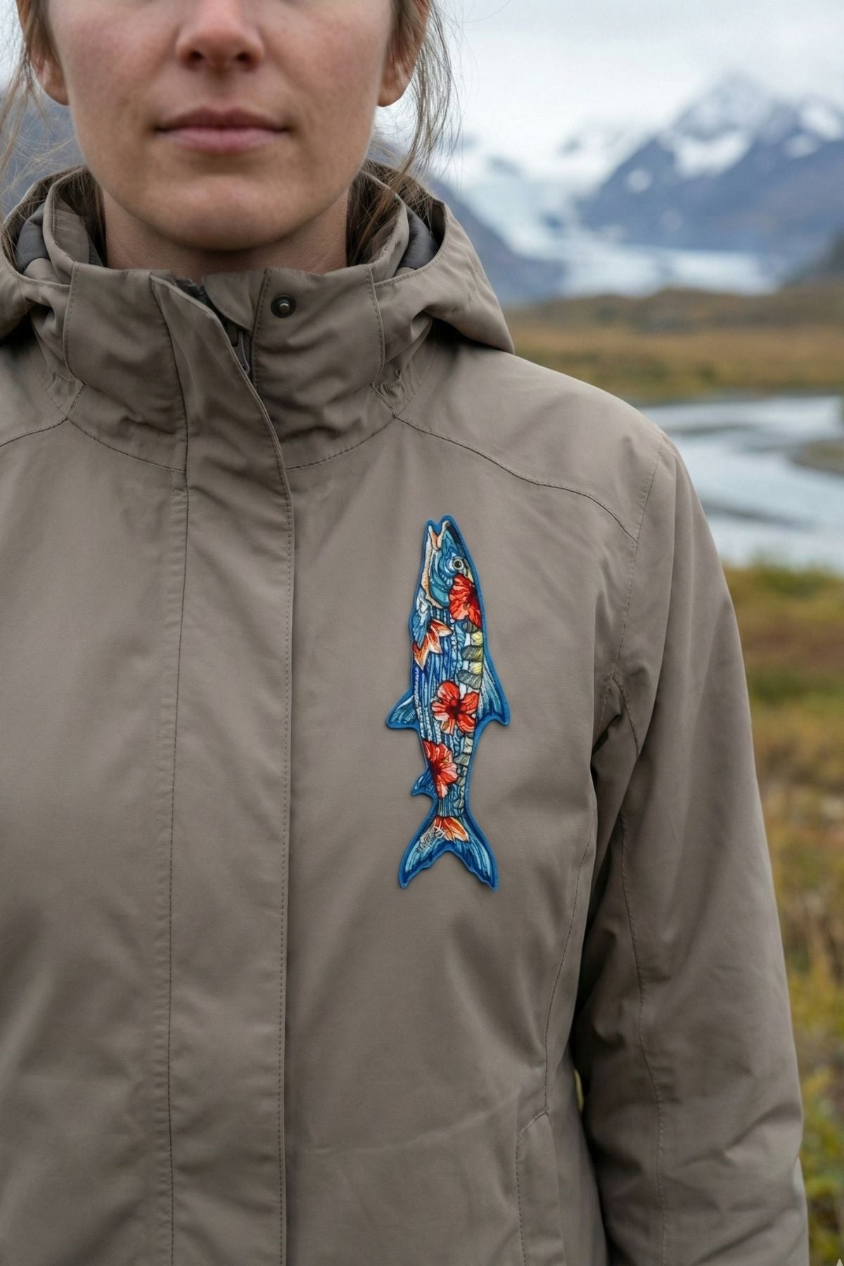 Person wearing a brown jacket with a colorful fish patch in a natural setting