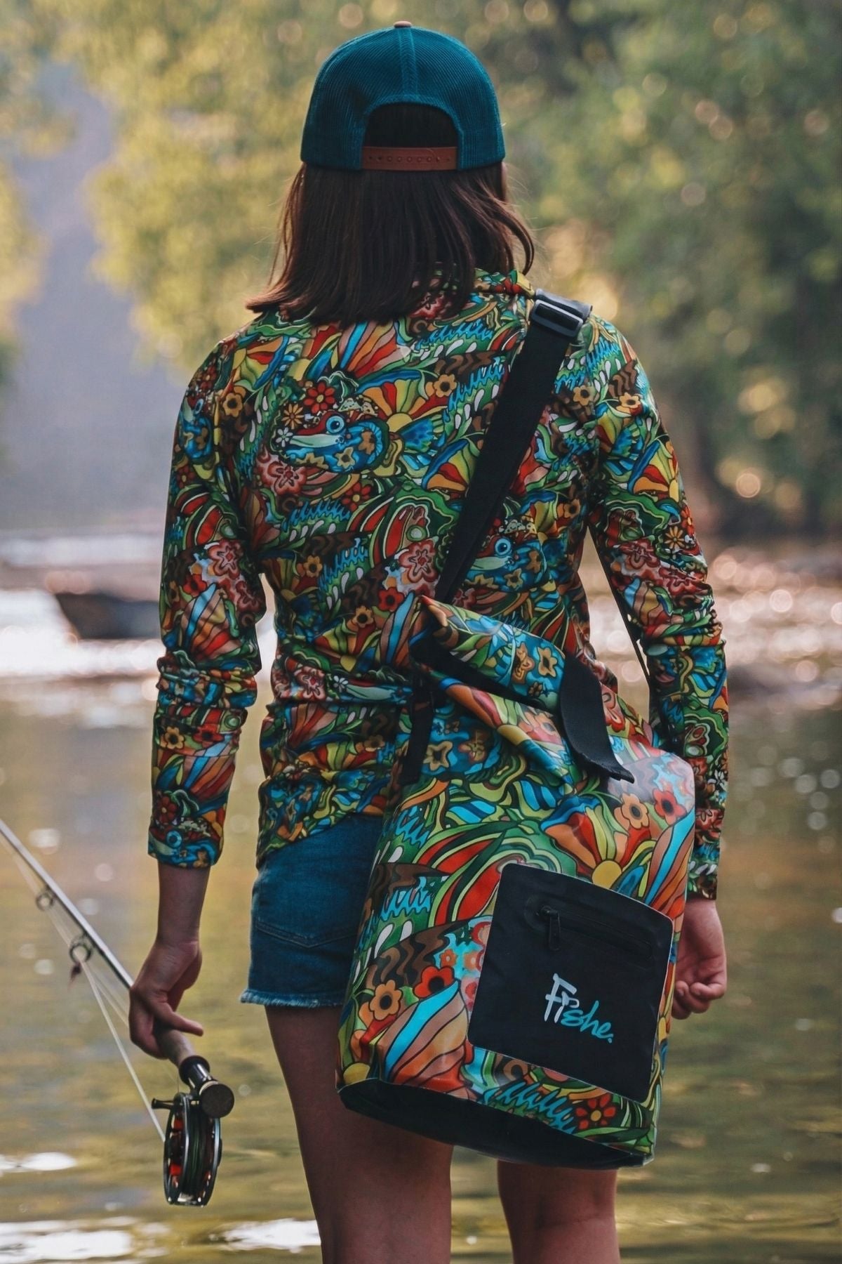 Person wearing a colorful patterned jacket and blue cap, holding a fishing rod by a body of water.