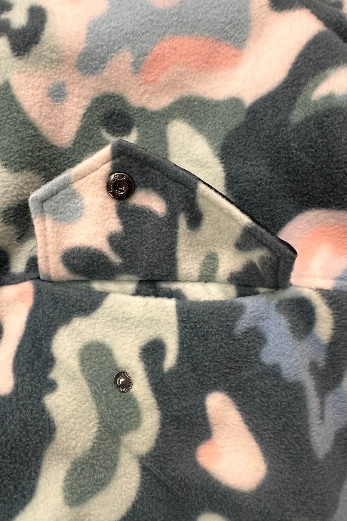 Close-up of a fleece jacket with a multicolor camouflage pattern in gray, green, black, and pink, featuring a buttoned flap pocket.