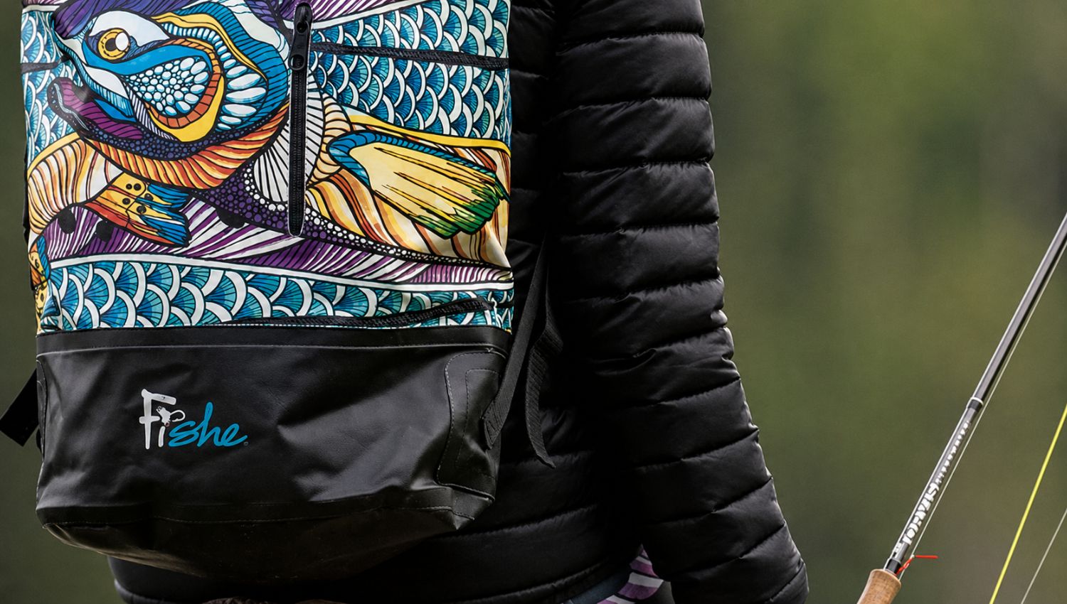 Person wearing a black jacket with colorful fish design, holding a fishing rod.
