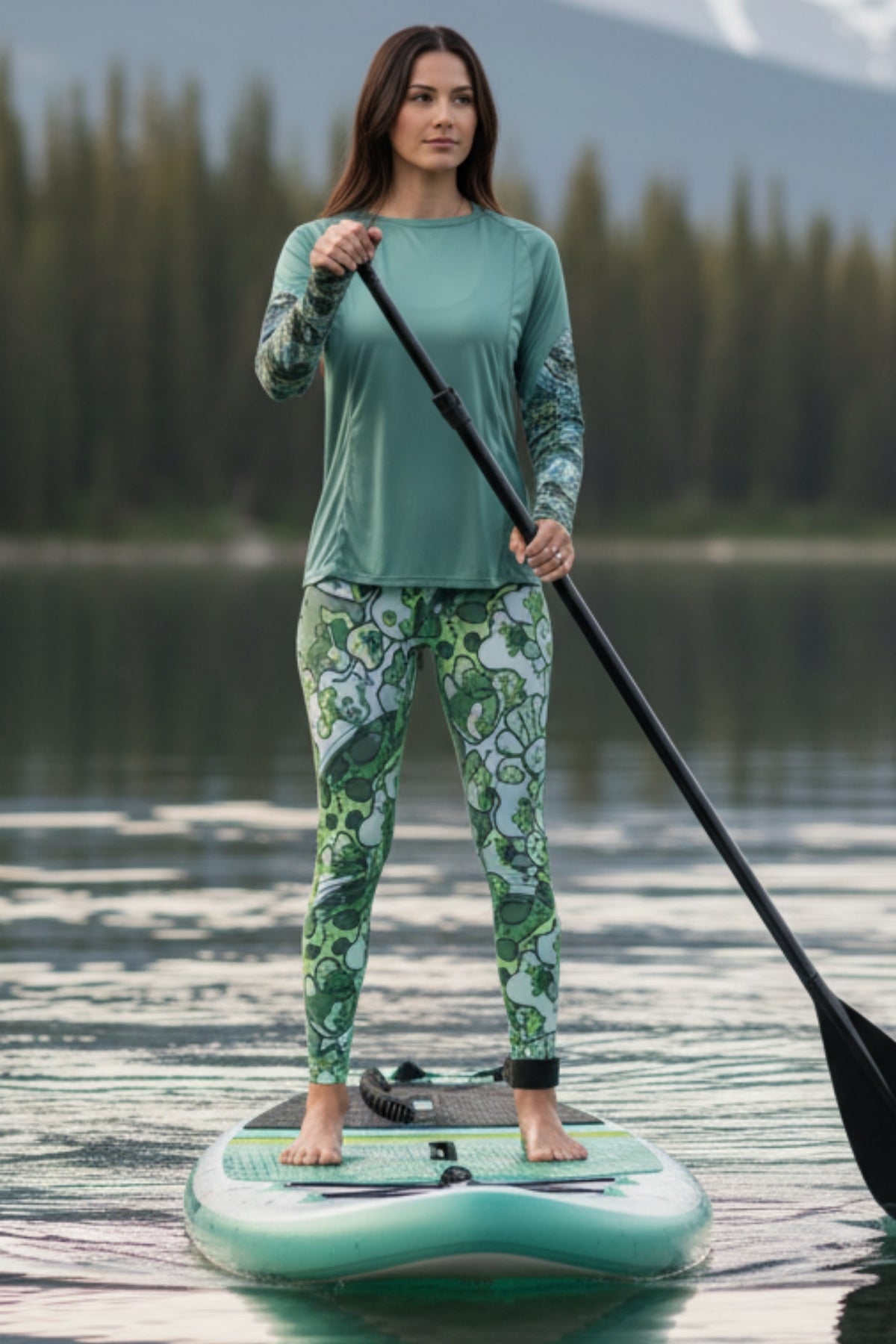 Woman paddleboarding on a lake wearing a green and white outfit.