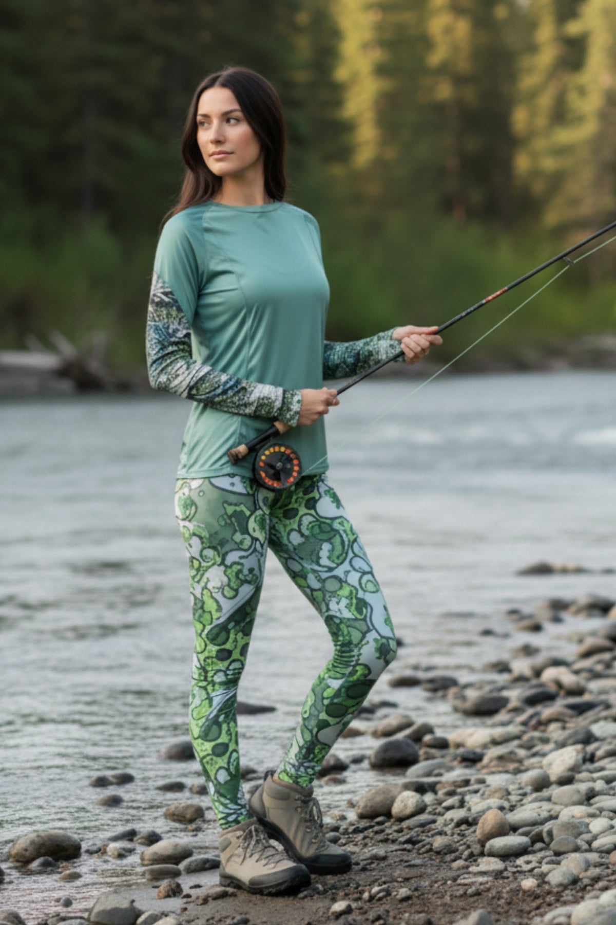 Woman fishing by a river wearing a green top and patterned leggings.