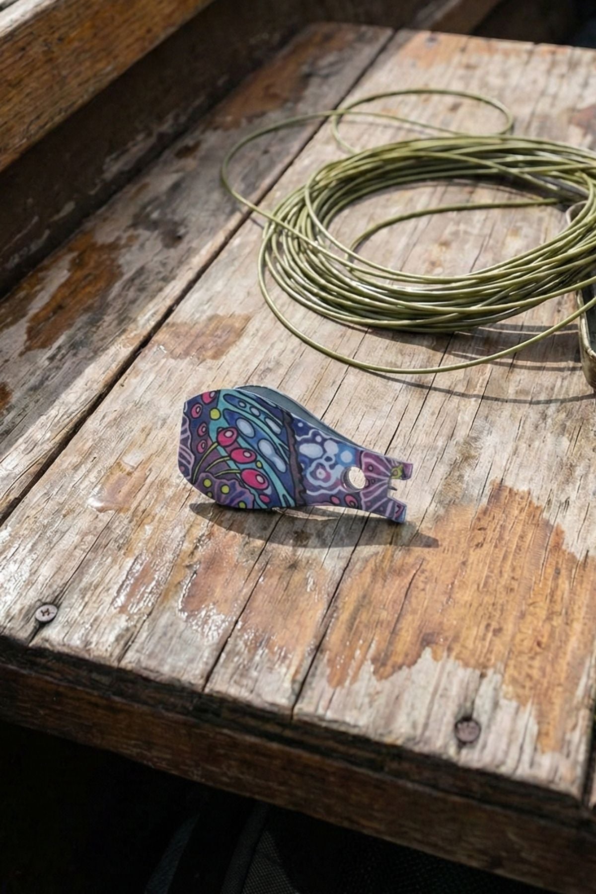 Colorful fish-shaped lure on a wooden surface with fishing line
