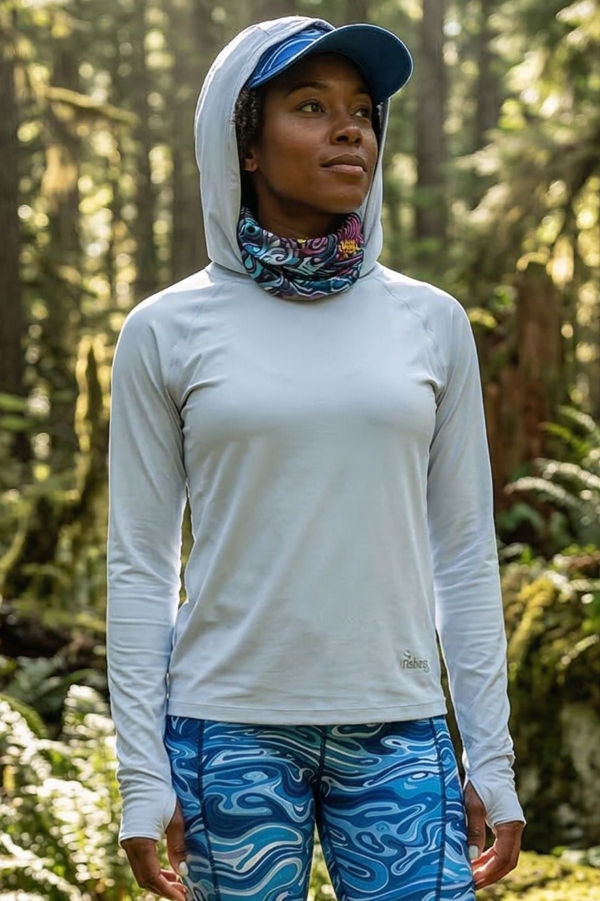 Person wearing a white long-sleeve shirt, blue cap, and patterned pants in a forest setting