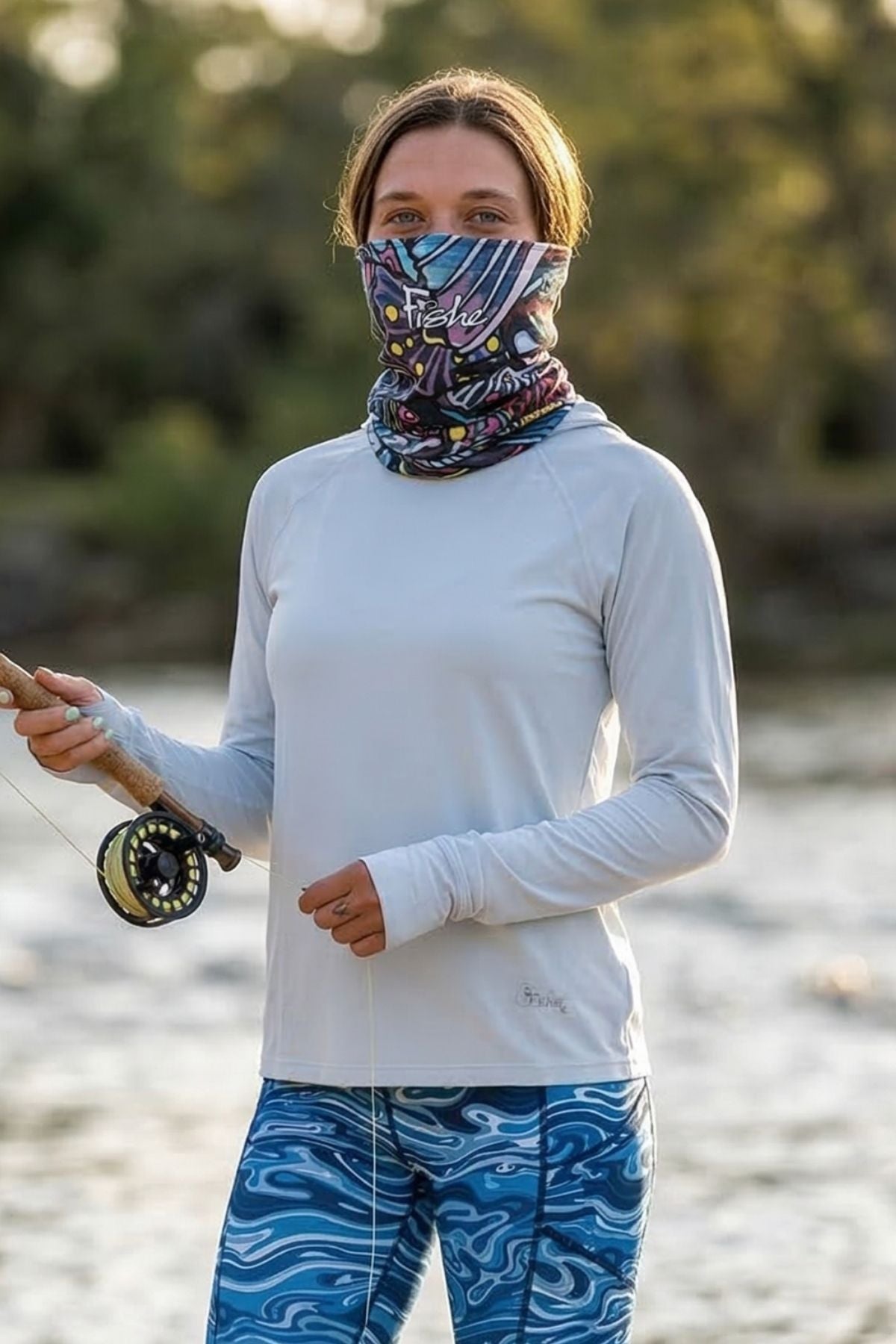 Person wearing a white long-sleeve shirt and blue patterned pants, holding a fishing rod by a body of water.
