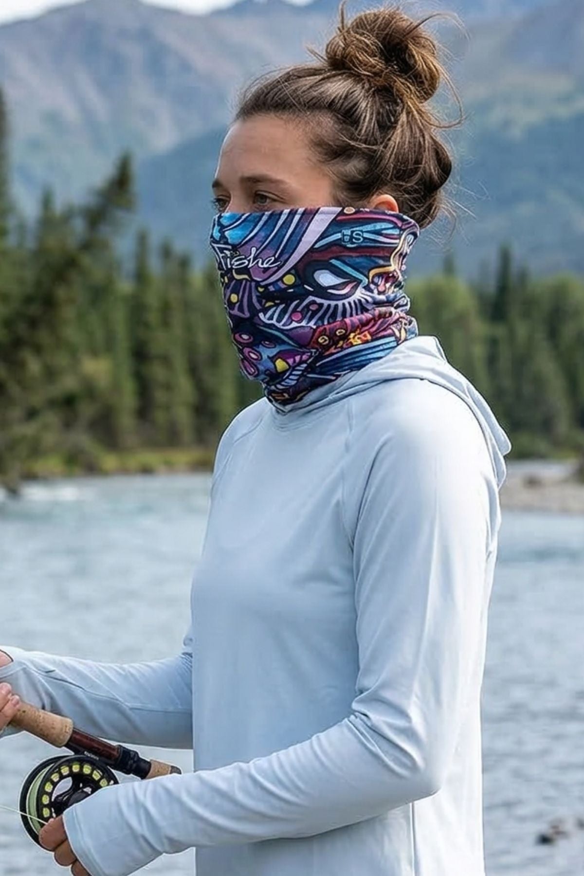 Person wearing a colorful neck gaiter by a lake with mountains in the background