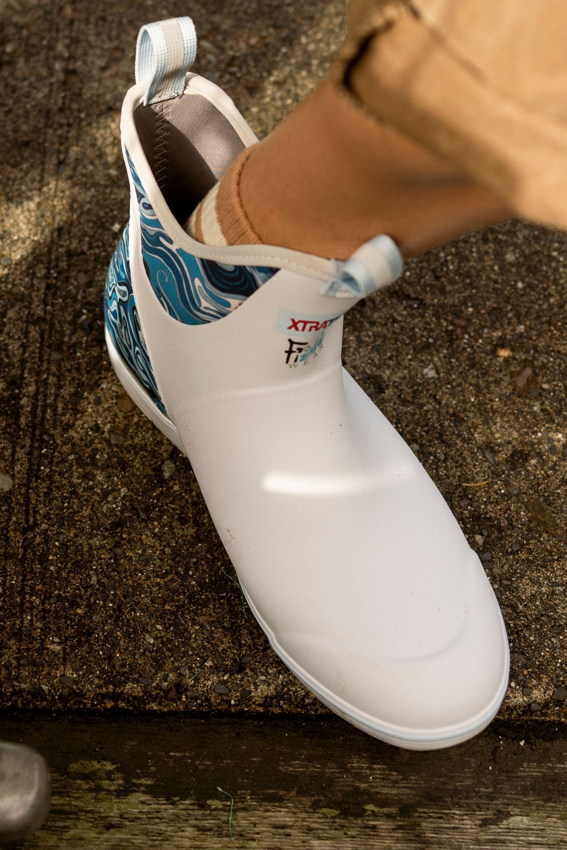 White slip-on shoe with blue patterned lining on a concrete surface