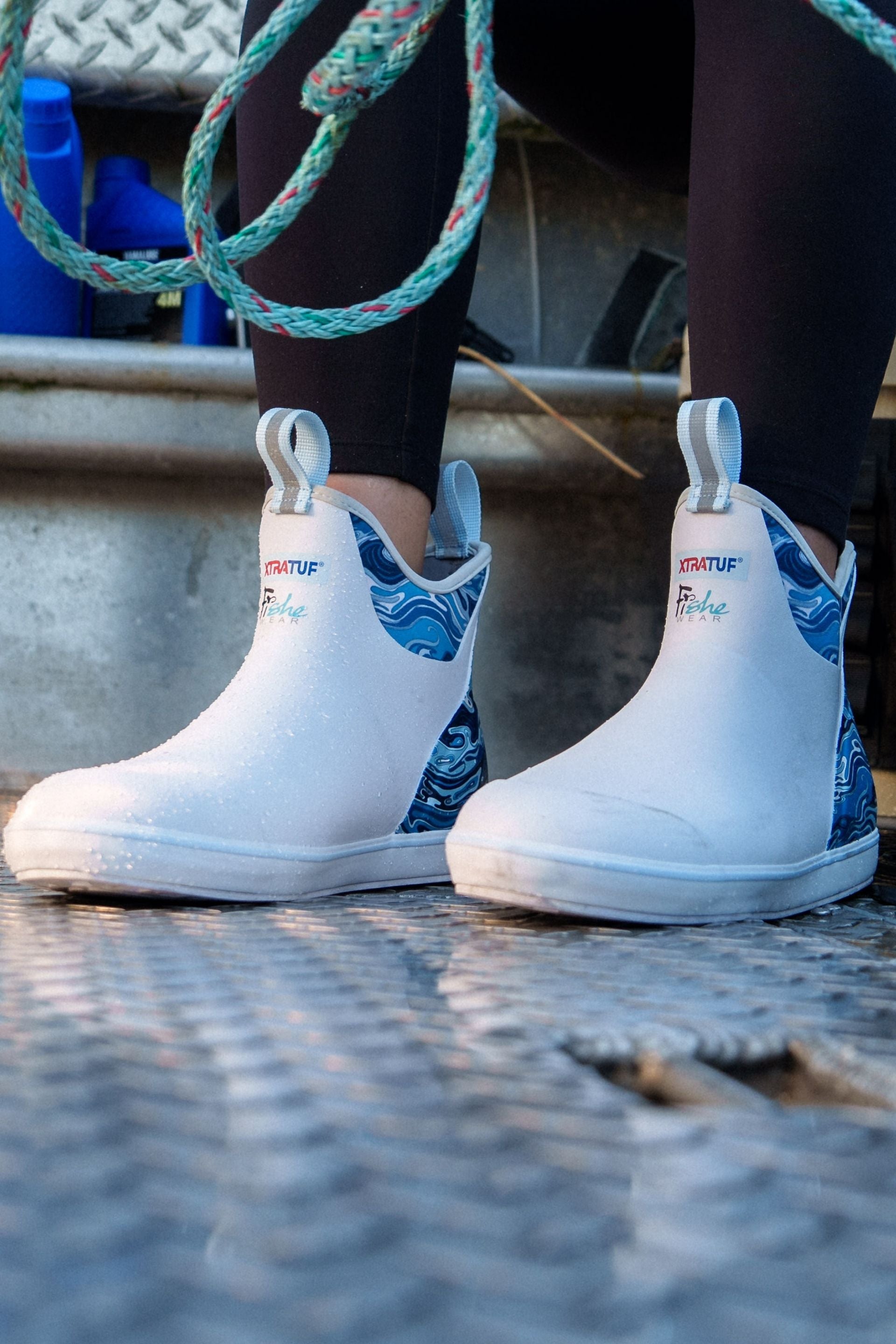 White rain boots with blue patterns worn by a person on a metal surface.