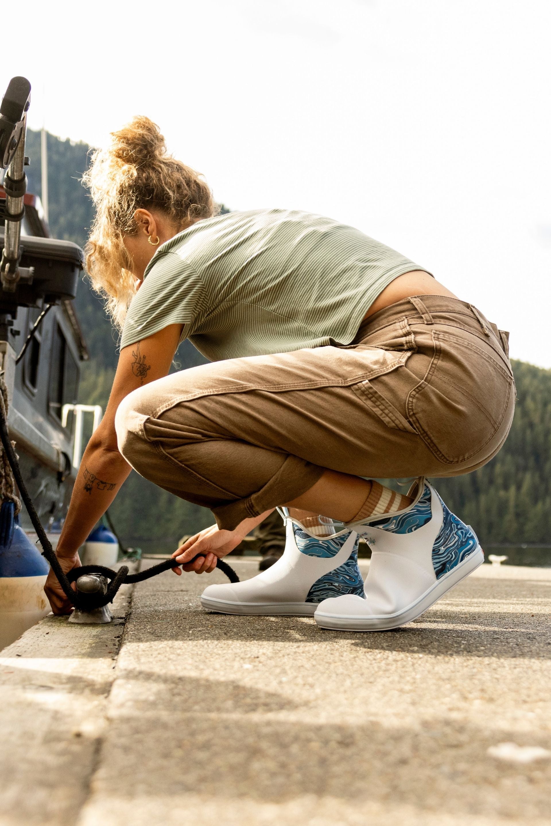 Person in green shirt and brown pants crouching outdoors with a scenic background