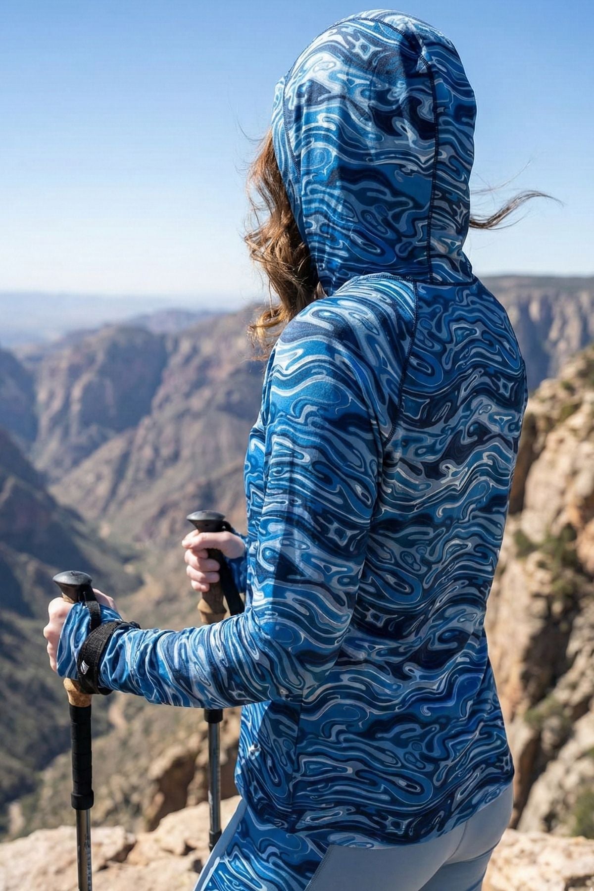 Person wearing a blue patterned jacket standing on a mountain with a scenic view.