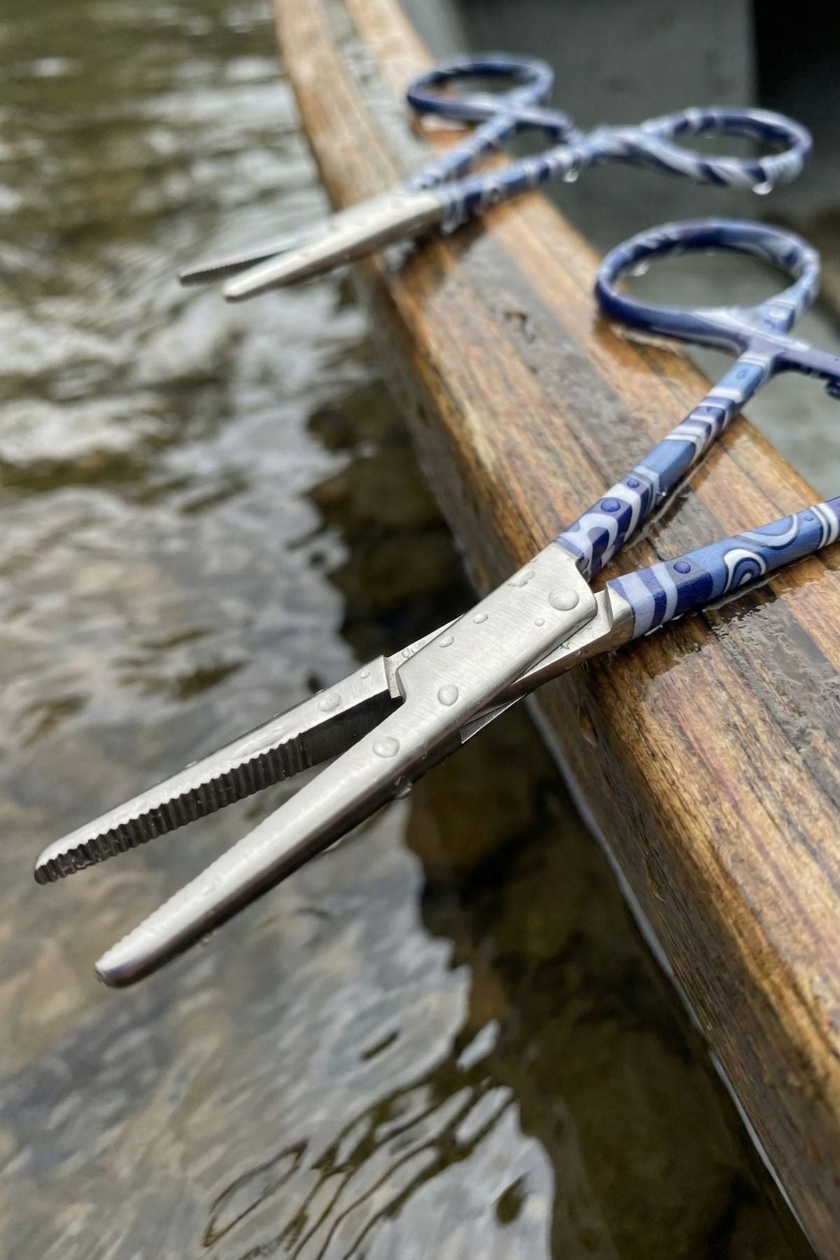 Pair of scissors with blue handles on a wooden surface near water