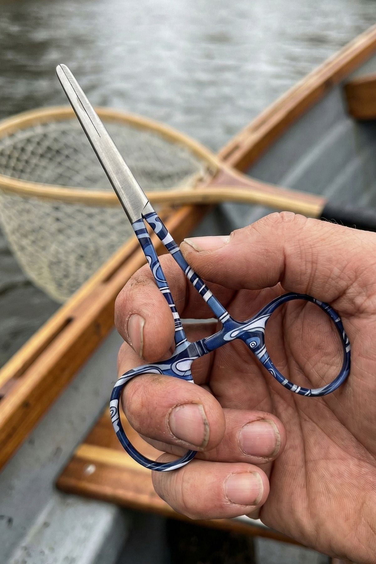 Hand holding a pair of blue-handled scissors with a blurred background