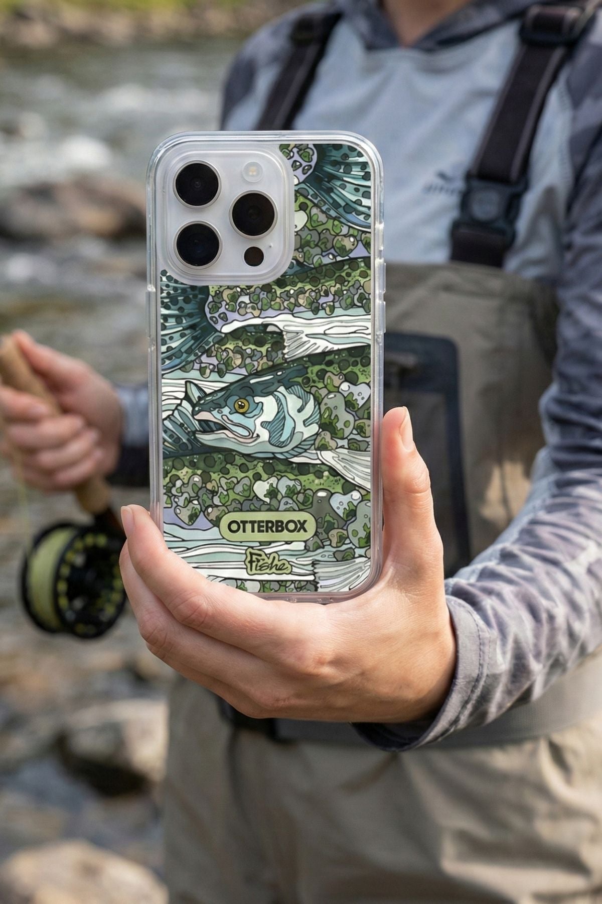 Person holding a phone with a fishing-themed case by OtterBox, outdoors.