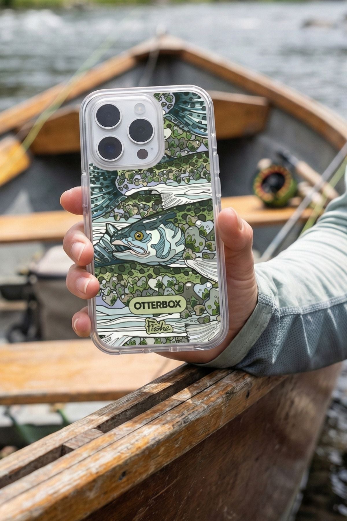 Person holding a phone case with nature design and OtterBox branding, background is a wooden boat on water.