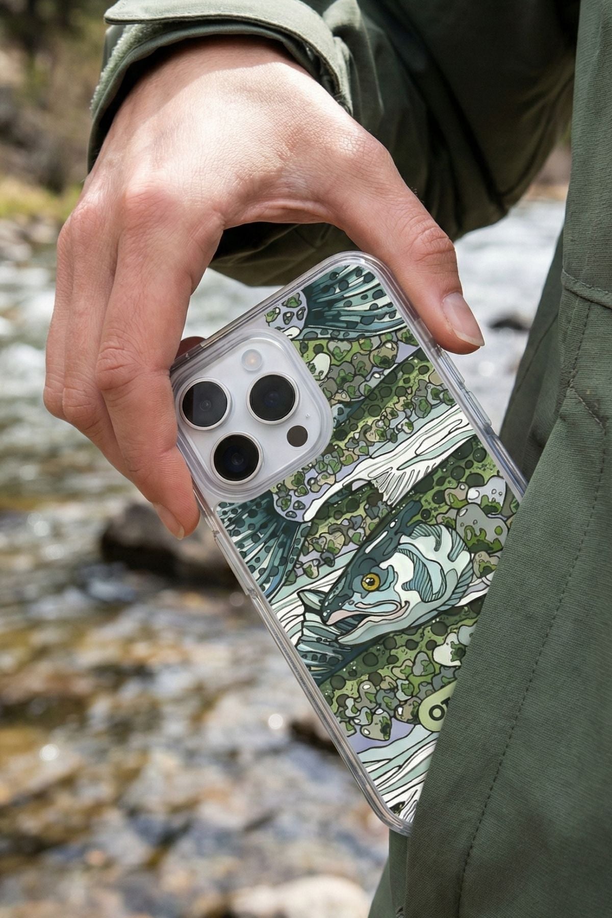 Phone case with fish design held by a person against a natural background