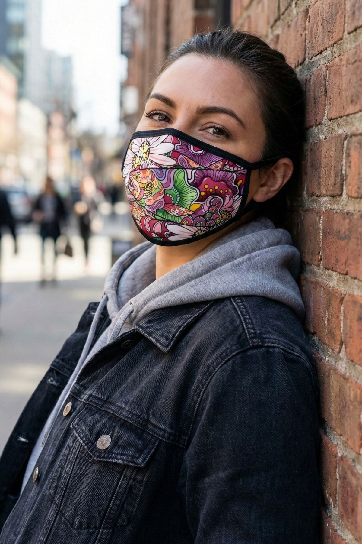 Person wearing a colorful face mask leaning against a brick wall.