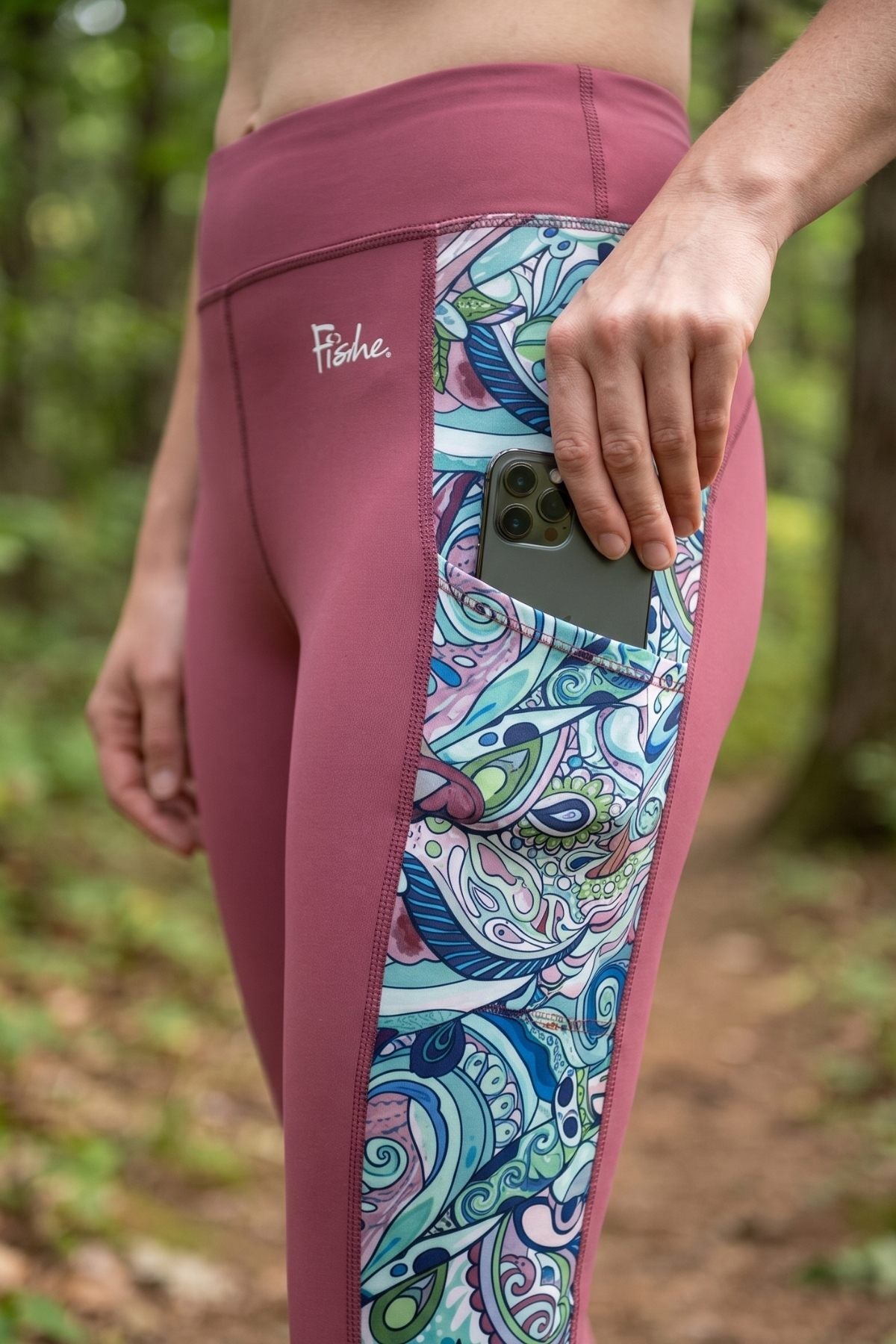 Pink leggings with colorful paisley pattern on side pocket held by a person in a forest setting.