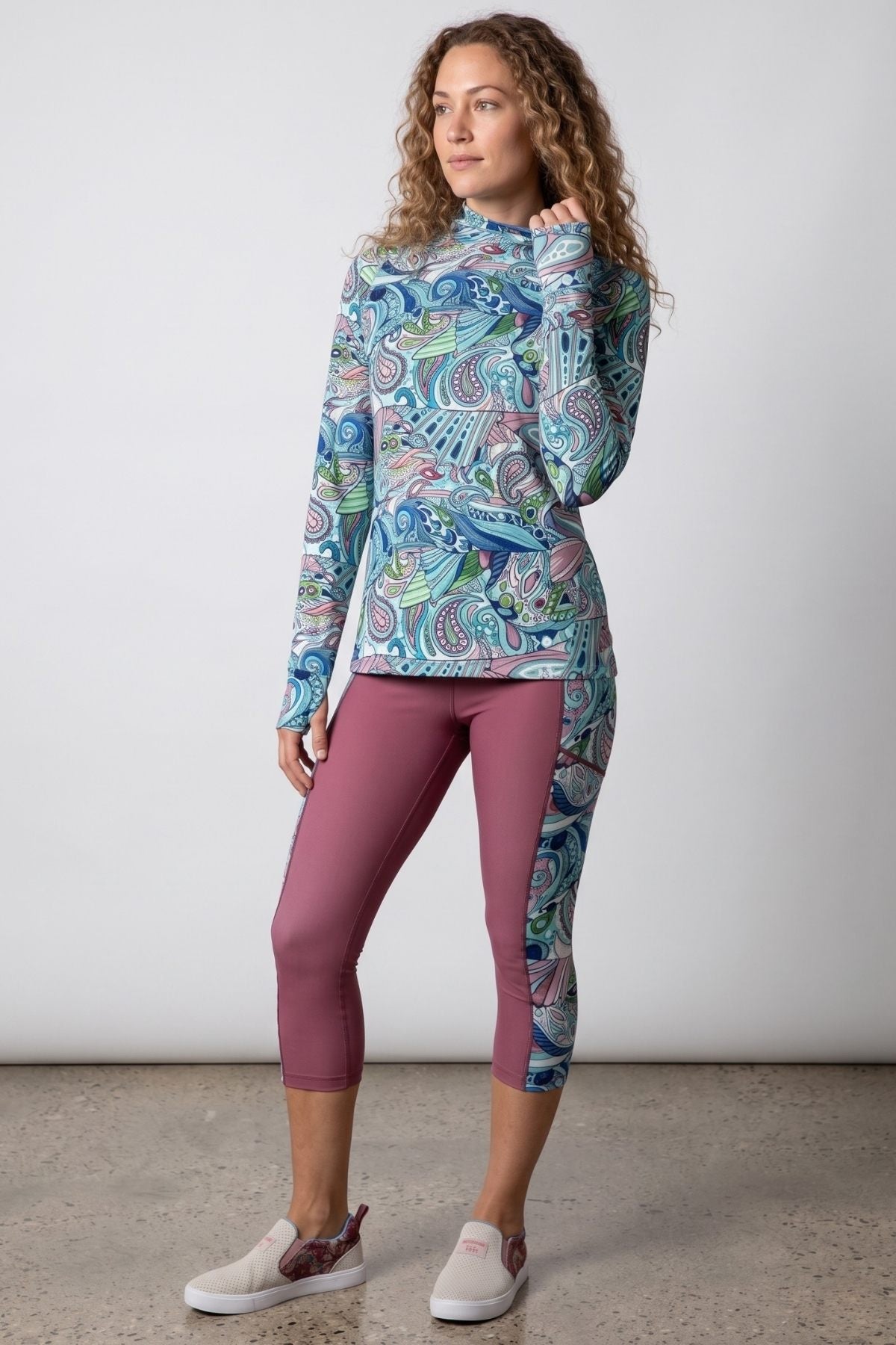 Woman wearing a colorful long-sleeve top and pink leggings against a white background