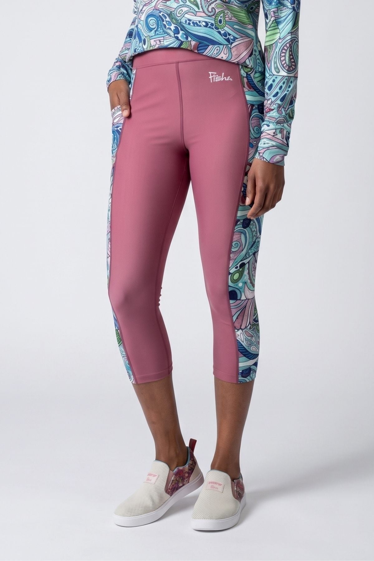 Person wearing pink leggings with a colorful patterned top and white sneakers on a light gray background