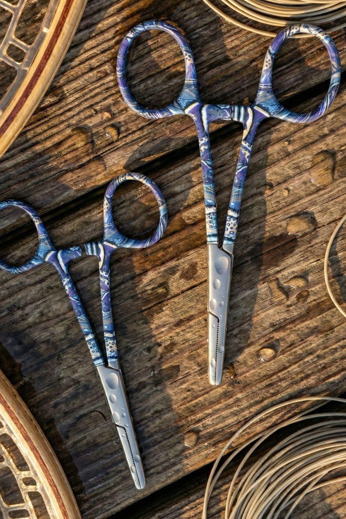 Pair of blue-handled scissors on a wooden surface with spools of thread.