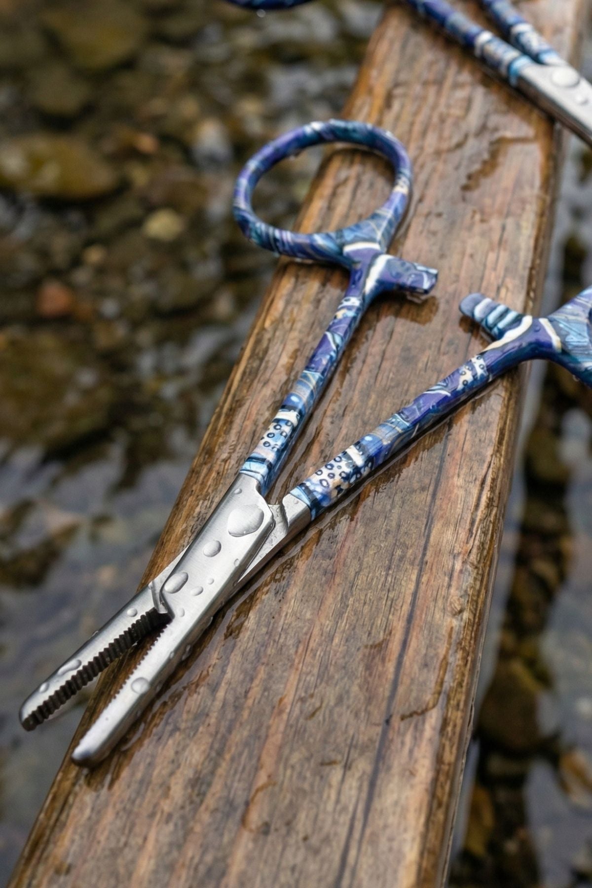 Fishing pliers with blue handles on a wooden surface near water