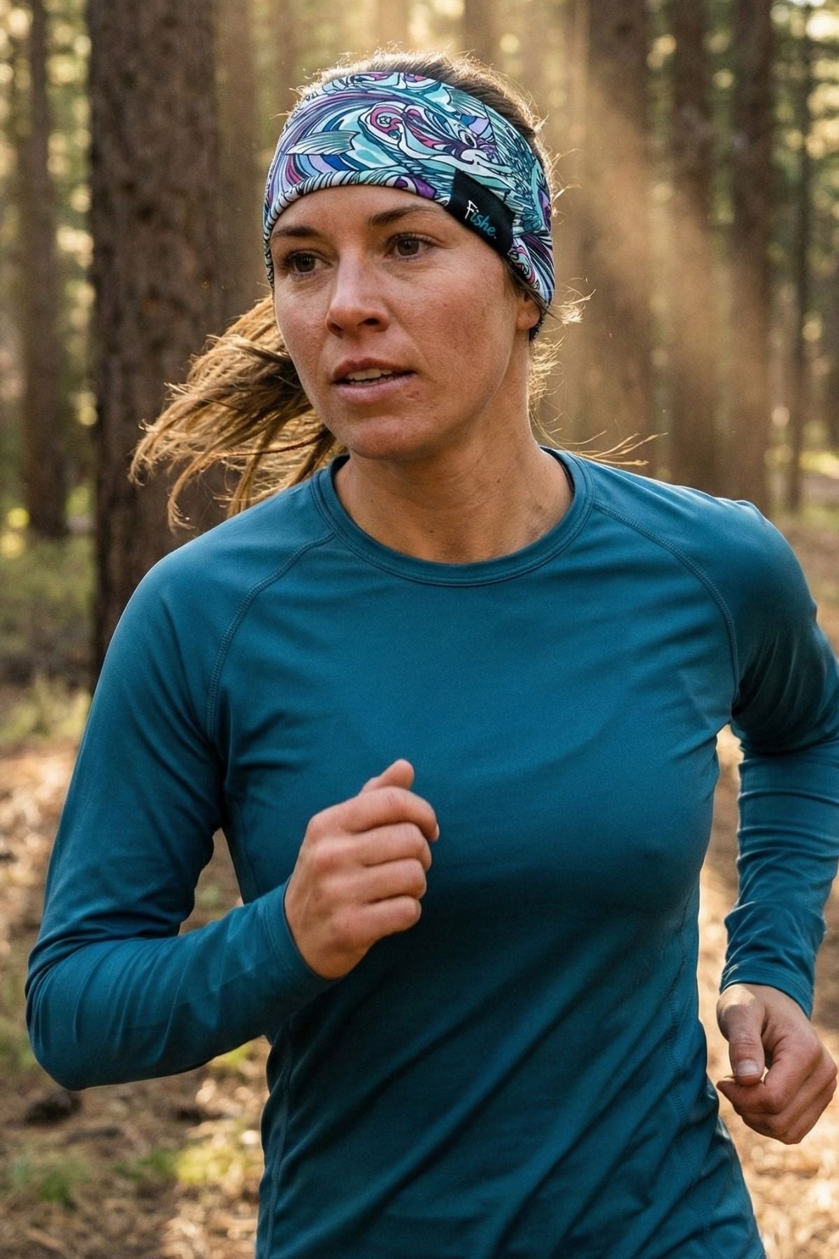 Woman running outdoors in a forest wearing a blue headband and long-sleeve shirt.