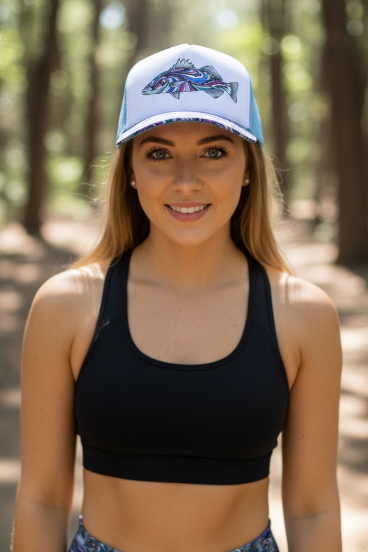 Woman wearing a black sports bra and blue cap with fish design in a forest setting