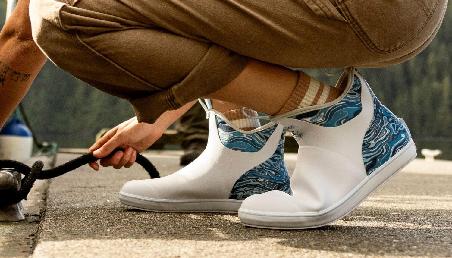 Person wearing white shoes with blue patterns, crouching on a road.