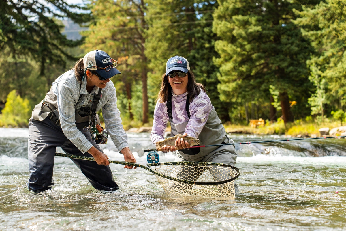 Two women wearing Casting for Recovery caps and sunglasses fly fishing together in a river