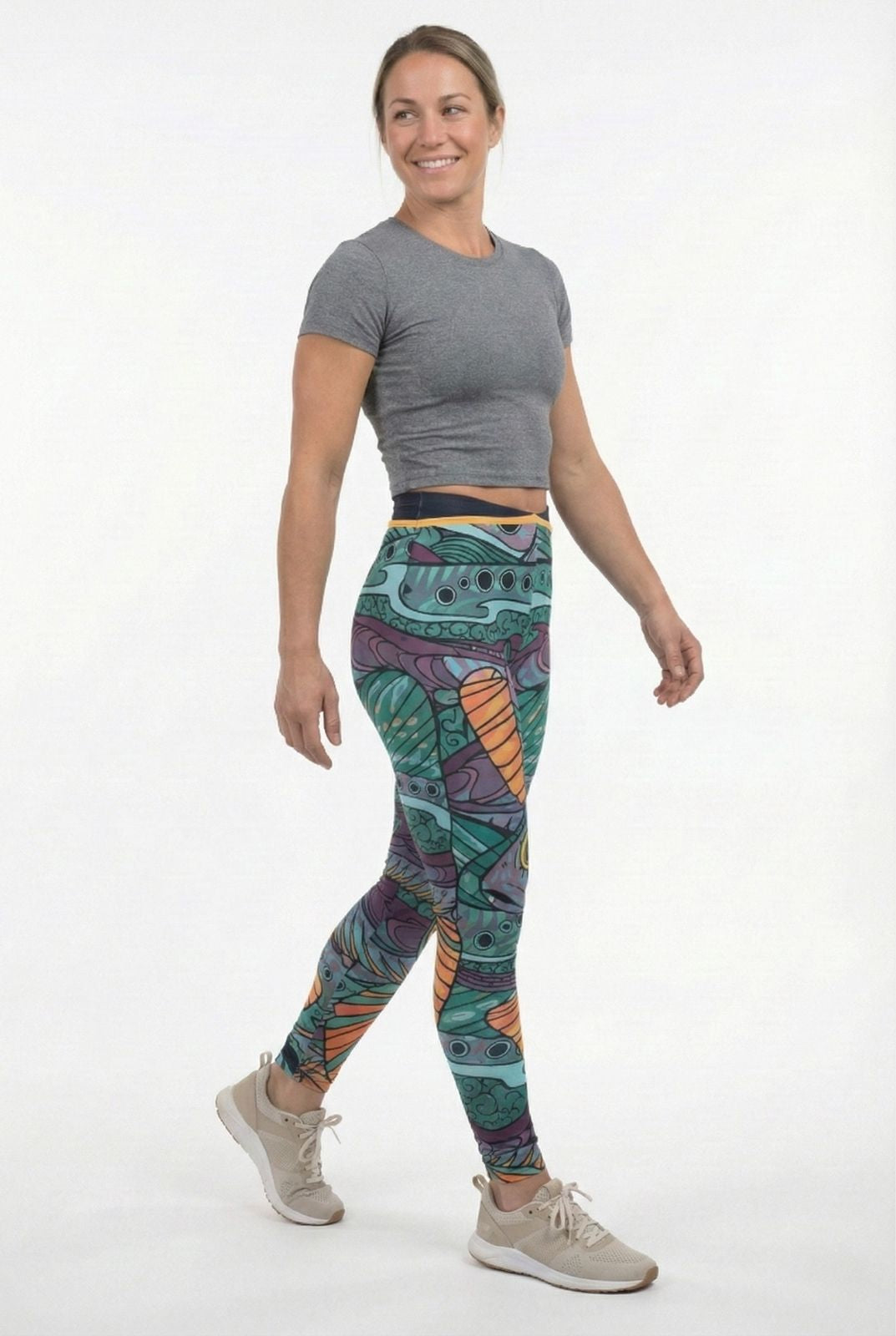 Woman wearing colorful patterned leggings and a gray crop top on a white background